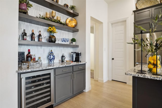 bar featuring gray cabinets, refrigerator, wine cooler, light hardwood / wood-style floors, and light stone countertops