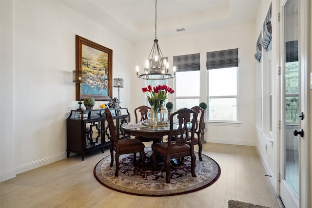 dining area with an inviting chandelier, a tray ceiling, and light hardwood / wood-style floors