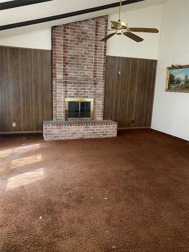 unfurnished living room featuring dark colored carpet, wood walls, lofted ceiling with beams, a brick fireplace, and ceiling fan