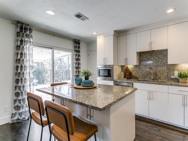 kitchen with visible vents, dark wood finished floors, appliances with stainless steel finishes, a sink, and backsplash