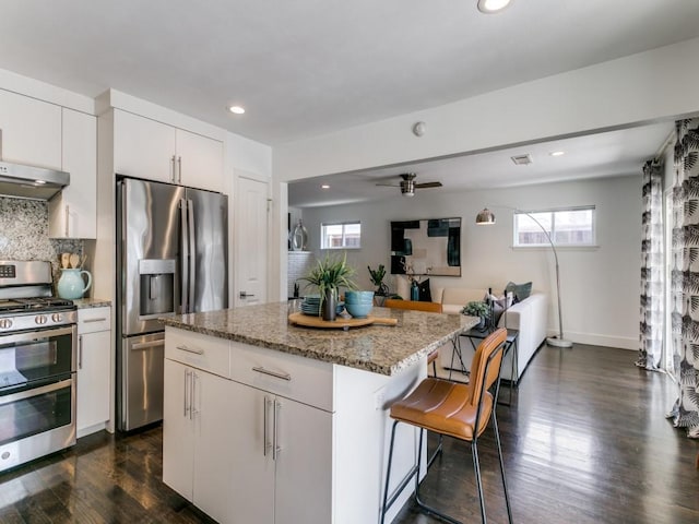 kitchen with a center island, dark wood-style flooring, a breakfast bar area, tasteful backsplash, and appliances with stainless steel finishes