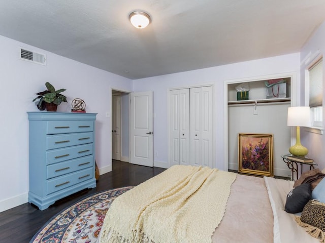 bedroom featuring baseboards, dark wood-type flooring, visible vents, and multiple closets