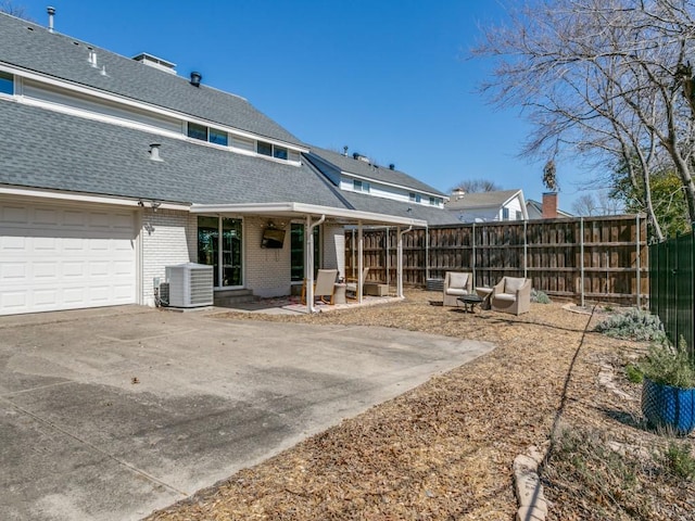 rear view of property featuring cooling unit, a shingled roof, brick siding, fence, and driveway