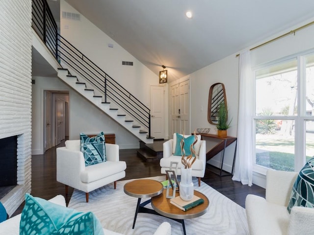 living room with a brick fireplace, stairs, visible vents, and wood finished floors