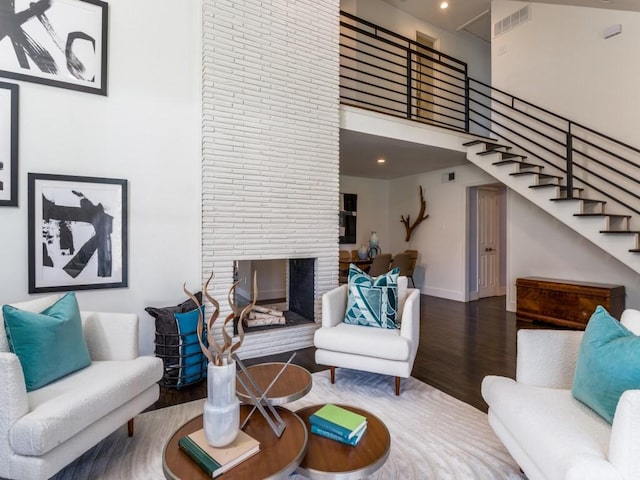 living room featuring a fireplace, visible vents, a high ceiling, wood finished floors, and stairs