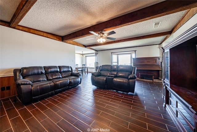 living room featuring beamed ceiling, ceiling fan, and a textured ceiling