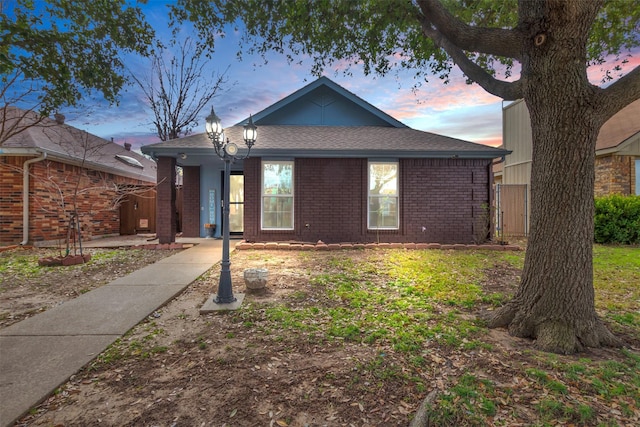 ranch-style home featuring fence, brick siding, and a shingled roof