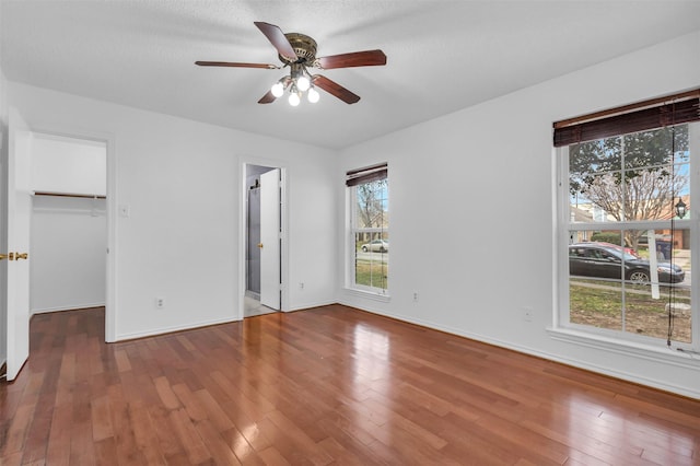 unfurnished bedroom featuring hardwood / wood-style flooring, ceiling fan, ensuite bathroom, and a spacious closet