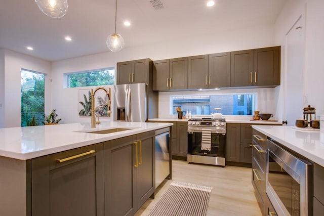 kitchen featuring sink, hanging light fixtures, appliances with stainless steel finishes, a kitchen island with sink, and light hardwood / wood-style floors