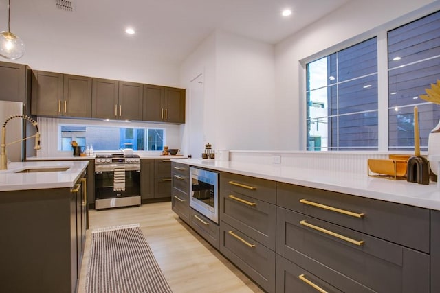 kitchen featuring sink, light hardwood / wood-style flooring, stainless steel appliances, dark brown cabinetry, and decorative light fixtures