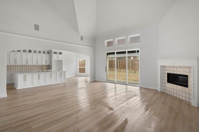 unfurnished living room with a tiled fireplace, sink, a towering ceiling, and light wood-type flooring