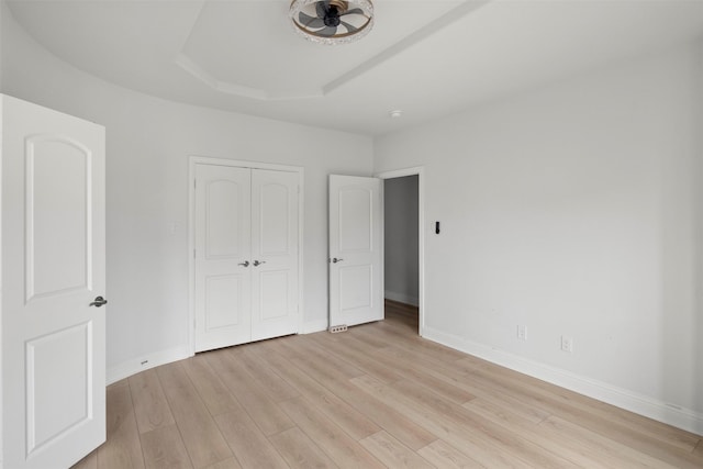 unfurnished bedroom with a closet, a raised ceiling, and light hardwood / wood-style flooring