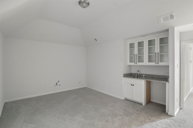 interior space with lofted ceiling, sink, white cabinets, light stone counters, and light carpet