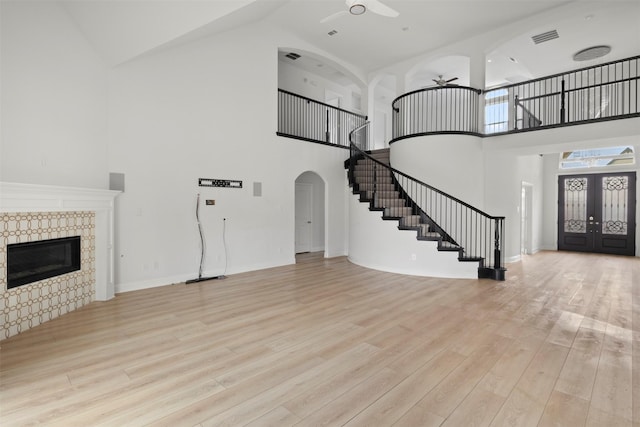 entrance foyer with french doors, high vaulted ceiling, light wood-type flooring, ceiling fan, and a fireplace