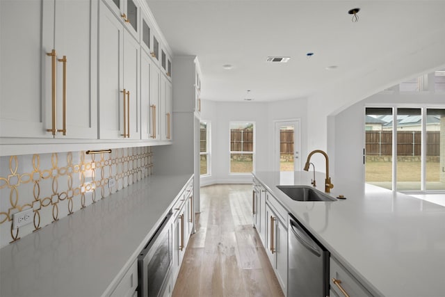 kitchen with sink, light wood-type flooring, dishwasher, white cabinets, and backsplash