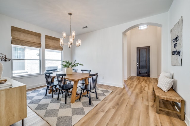 dining room with arched walkways, light wood-style flooring, baseboards, and an inviting chandelier