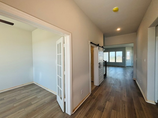 hallway with a barn door, dark wood-style floors, and baseboards