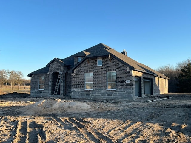 view of front of home with brick siding, a chimney, an attached garage, and roof with shingles