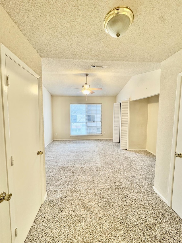 empty room featuring ceiling fan, carpet flooring, vaulted ceiling, and a textured ceiling