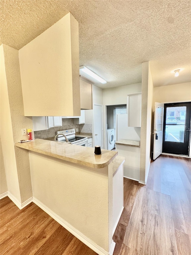 kitchen featuring white range with electric cooktop, white cabinetry, washer / dryer, kitchen peninsula, and light wood-type flooring