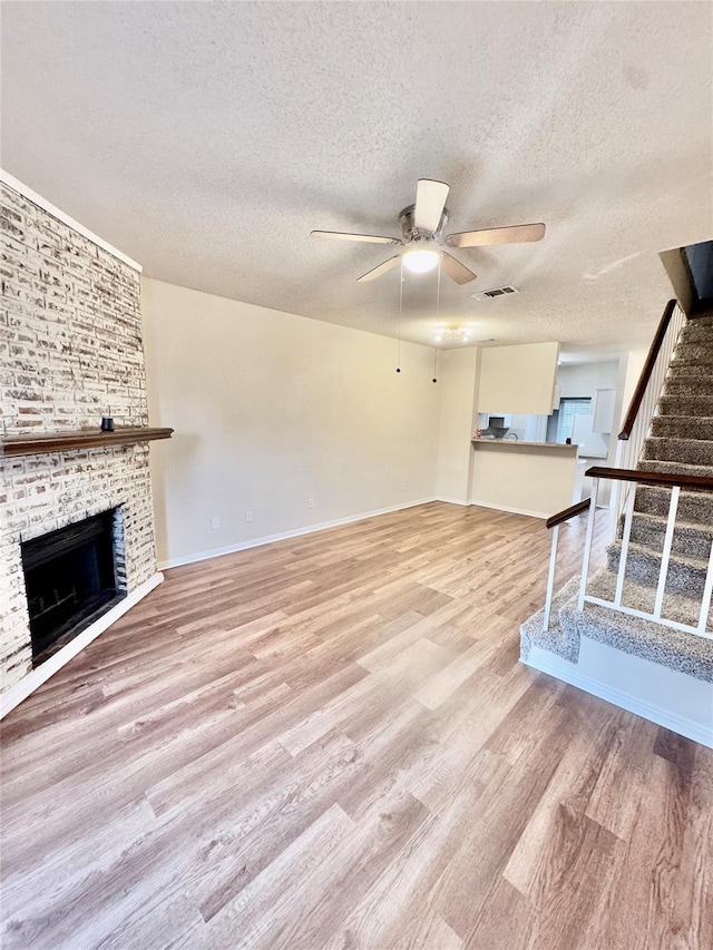 unfurnished living room featuring ceiling fan, a textured ceiling, a brick fireplace, and light hardwood / wood-style flooring