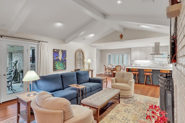 living room featuring vaulted ceiling with beams, sink, and light hardwood / wood-style flooring