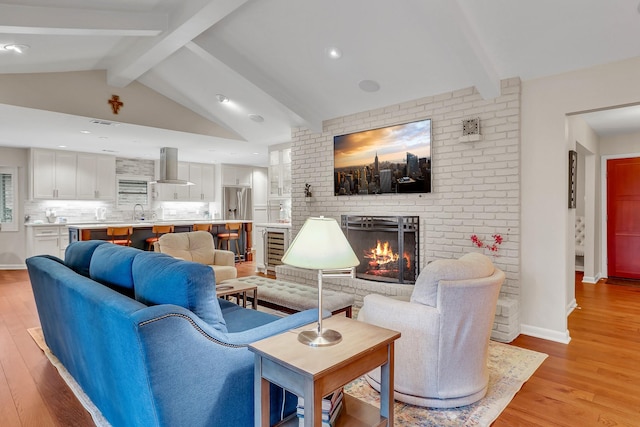 living room with sink, a fireplace, lofted ceiling with beams, and light wood-type flooring