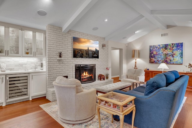 living room with vaulted ceiling with beams, a fireplace, beverage cooler, and light wood-type flooring