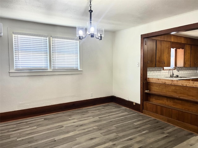 unfurnished dining area with dark hardwood / wood-style floors, sink, a textured ceiling, and a notable chandelier