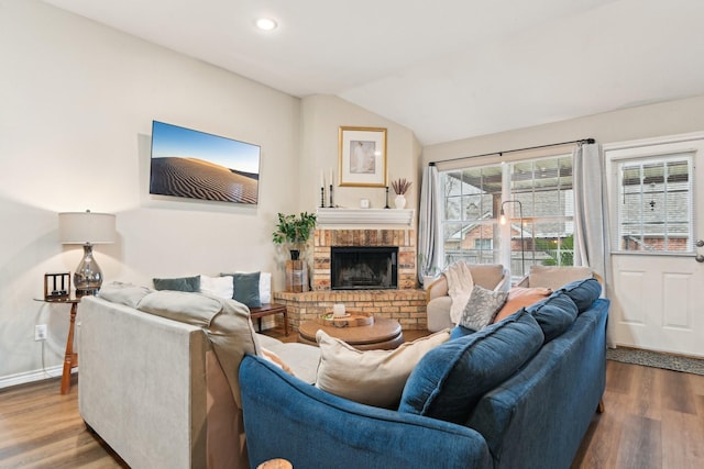 living room featuring vaulted ceiling, hardwood / wood-style floors, and a brick fireplace