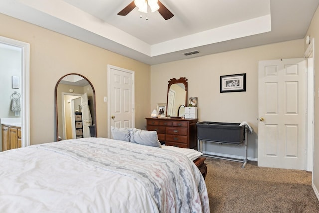 carpeted bedroom with ceiling fan, ensuite bathroom, and a raised ceiling