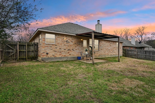 back house at dusk featuring a patio area and a lawn