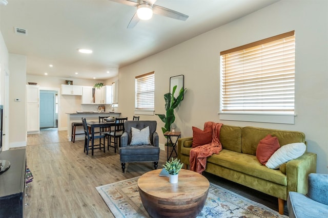 living area featuring visible vents, baseboards, light wood-style floors, and ceiling fan