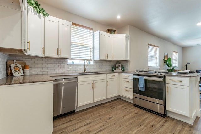 kitchen featuring a peninsula, a sink, light wood-style floors, appliances with stainless steel finishes, and white cabinetry