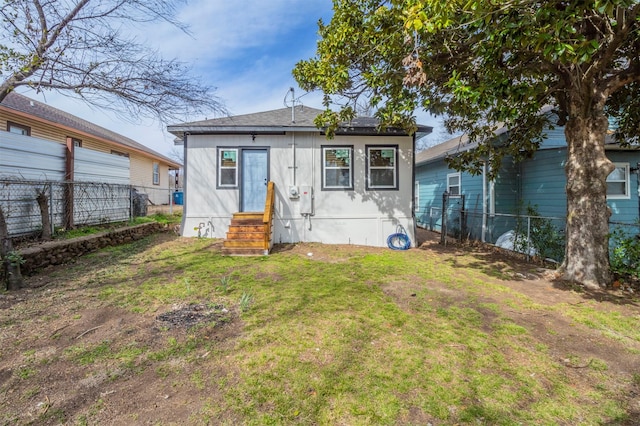 back of house with entry steps, a lawn, and fence