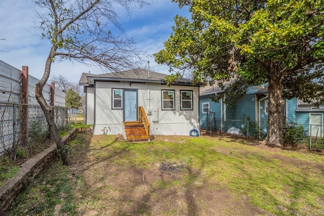 rear view of house featuring entry steps, a fenced backyard, and a lawn