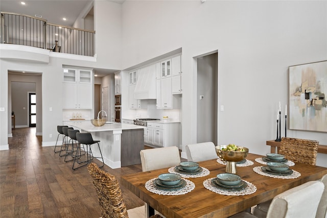 dining area featuring dark wood-type flooring, recessed lighting, baseboards, and a towering ceiling