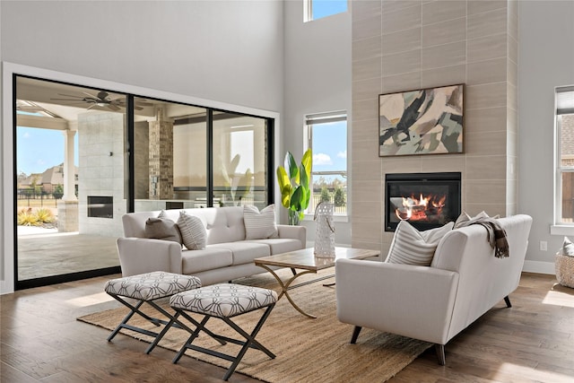 living area with baseboards, ceiling fan, a tile fireplace, a high ceiling, and wood finished floors