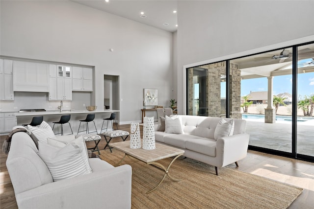 living area featuring baseboards, recessed lighting, ceiling fan, a towering ceiling, and light wood-type flooring