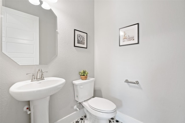 half bath with a sink, baseboards, and toilet