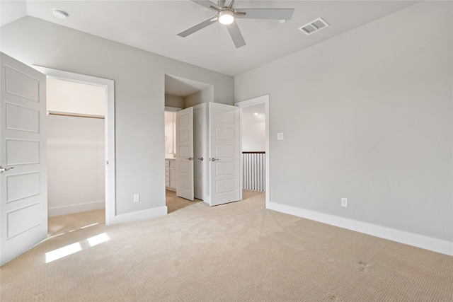 unfurnished bedroom featuring visible vents, light carpet, a walk in closet, connected bathroom, and baseboards