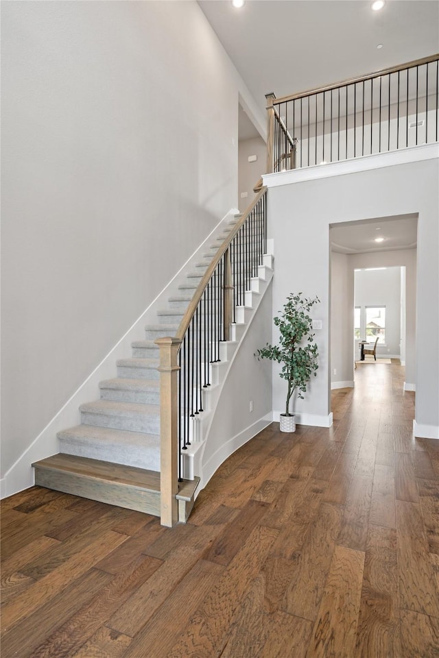 staircase featuring recessed lighting, baseboards, a high ceiling, and hardwood / wood-style floors