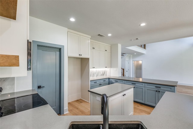 kitchen featuring sink, light hardwood / wood-style flooring, kitchen peninsula, and white cabinets