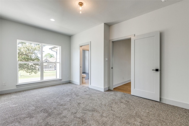 unfurnished bedroom with ensuite bathroom and light carpet