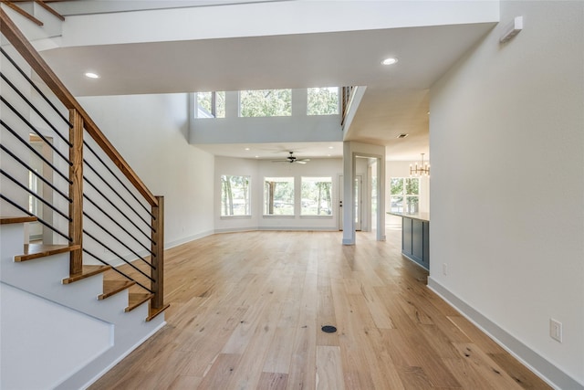 unfurnished living room with ceiling fan with notable chandelier and light hardwood / wood-style floors