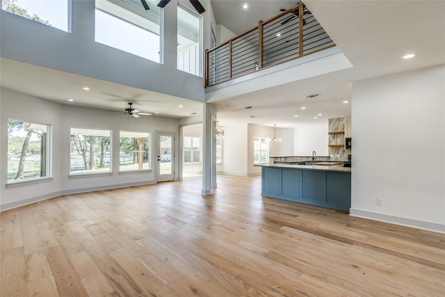 unfurnished living room featuring a healthy amount of sunlight, ceiling fan with notable chandelier, and light wood-type flooring