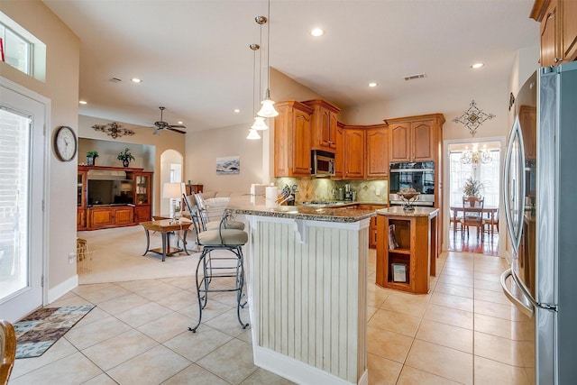 kitchen featuring a breakfast bar, decorative light fixtures, light tile patterned floors, appliances with stainless steel finishes, and light stone countertops