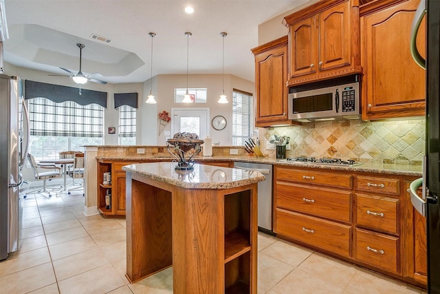 kitchen with appliances with stainless steel finishes, a center island, a tray ceiling, decorative light fixtures, and kitchen peninsula