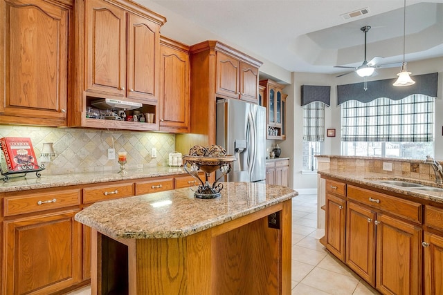 kitchen featuring sink, light stone counters, stainless steel fridge, a raised ceiling, and a kitchen island