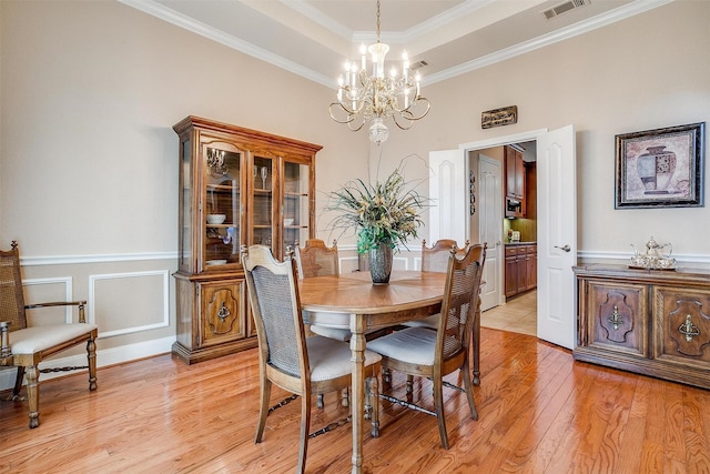 dining space featuring crown molding, a chandelier, light hardwood / wood-style floors, and a tray ceiling